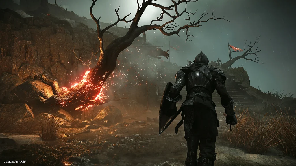 a screenshot of the game Demon Souls that shows a character in metal armour walking beside a burning tree